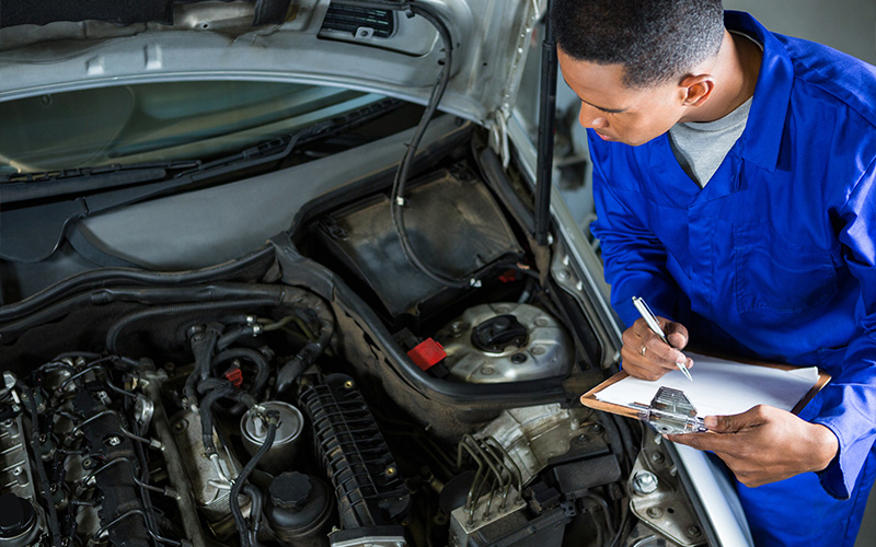 A professional mechanic in blue overalls performing a car engine inspection