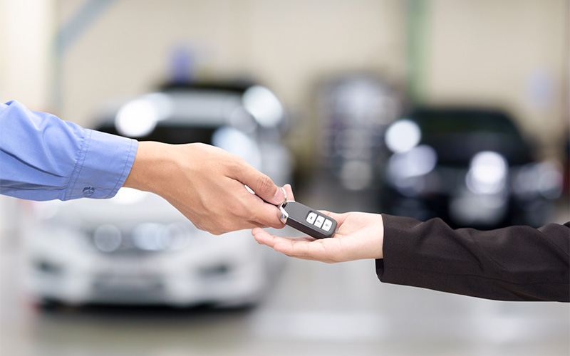 Hands exchange car key fob in dealership setting.
