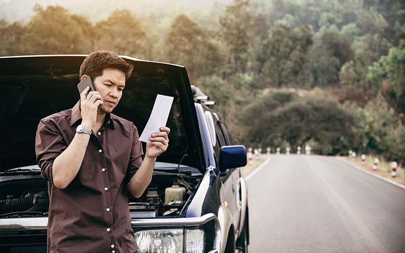 Distressed driver holding traffic summons letter beside parked vehicle.
