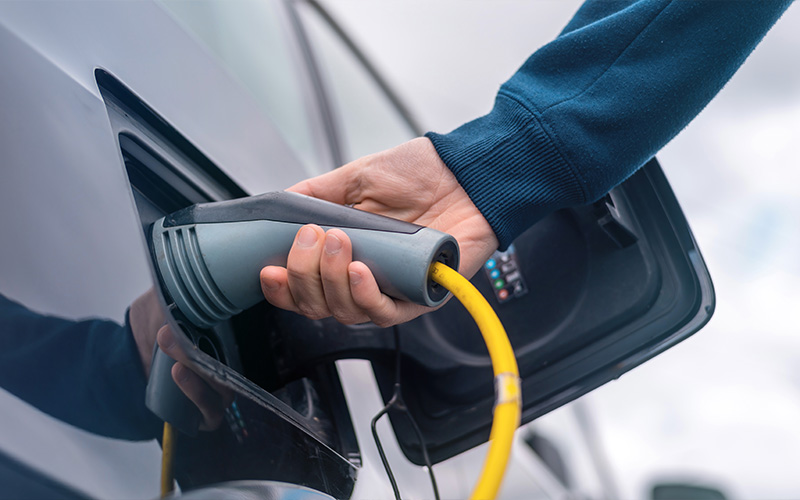 Driver connecting fast-charging cable to electric vehicle charging port.