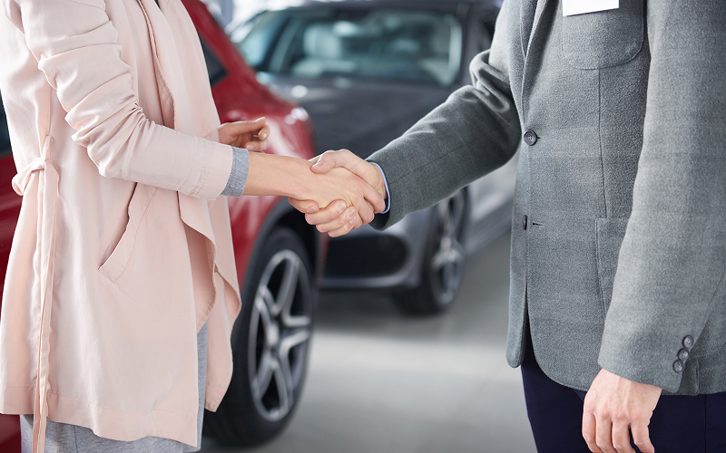 Salesman and woman handshaking after agreeing to sell car